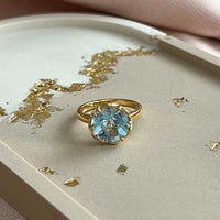 Flore - gouden flowercup ring blauwe topaas